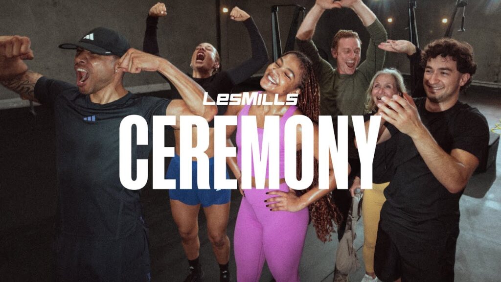Groupe joyeux célébrant le programme Les Mills Ceremony en tenue Adidas, muscles fléchis et sourires.